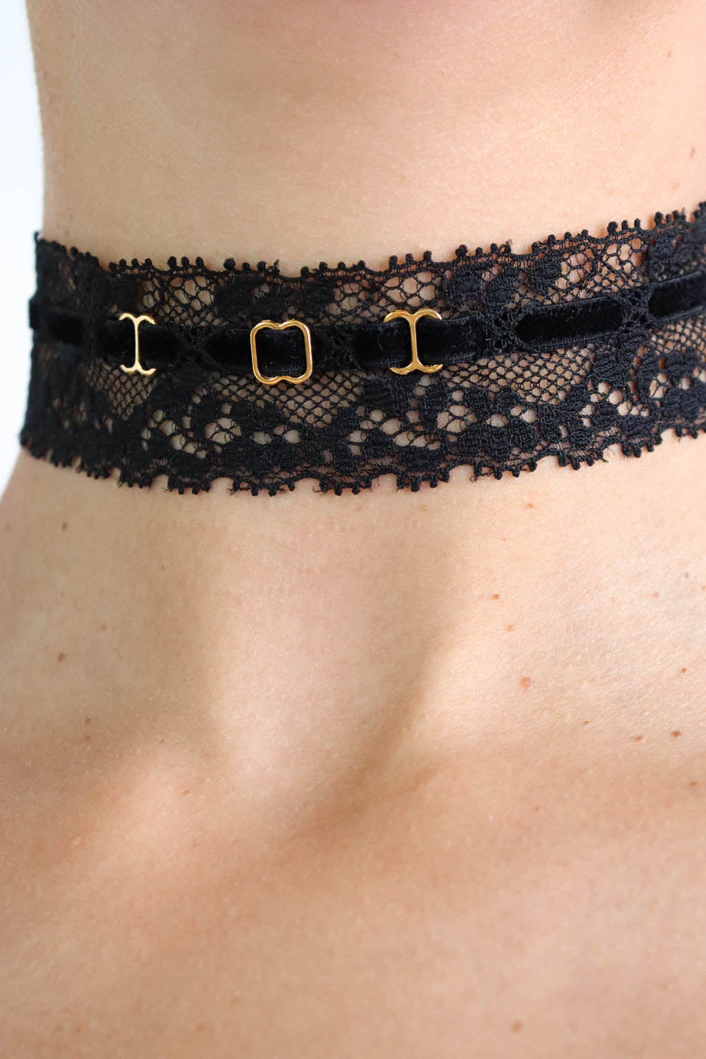 Close up view of a black choker made with fie lace band, soft velvet strap and gold hardware.