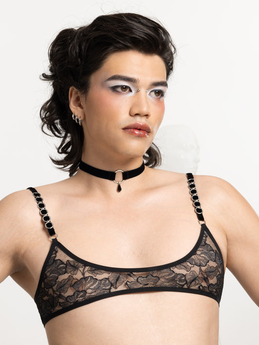 Model wearing a black velvet choker made with an adjustable strap and a silver o-ring charm attached to a black crystal pendant. Also wearing a lace micro bralette.