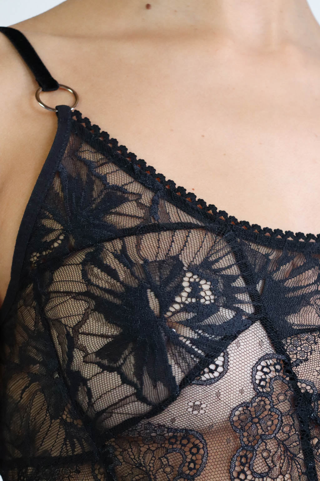 Close up view of the floral lace details on a black crop-top with adjustable velvet straps and silver hardware.