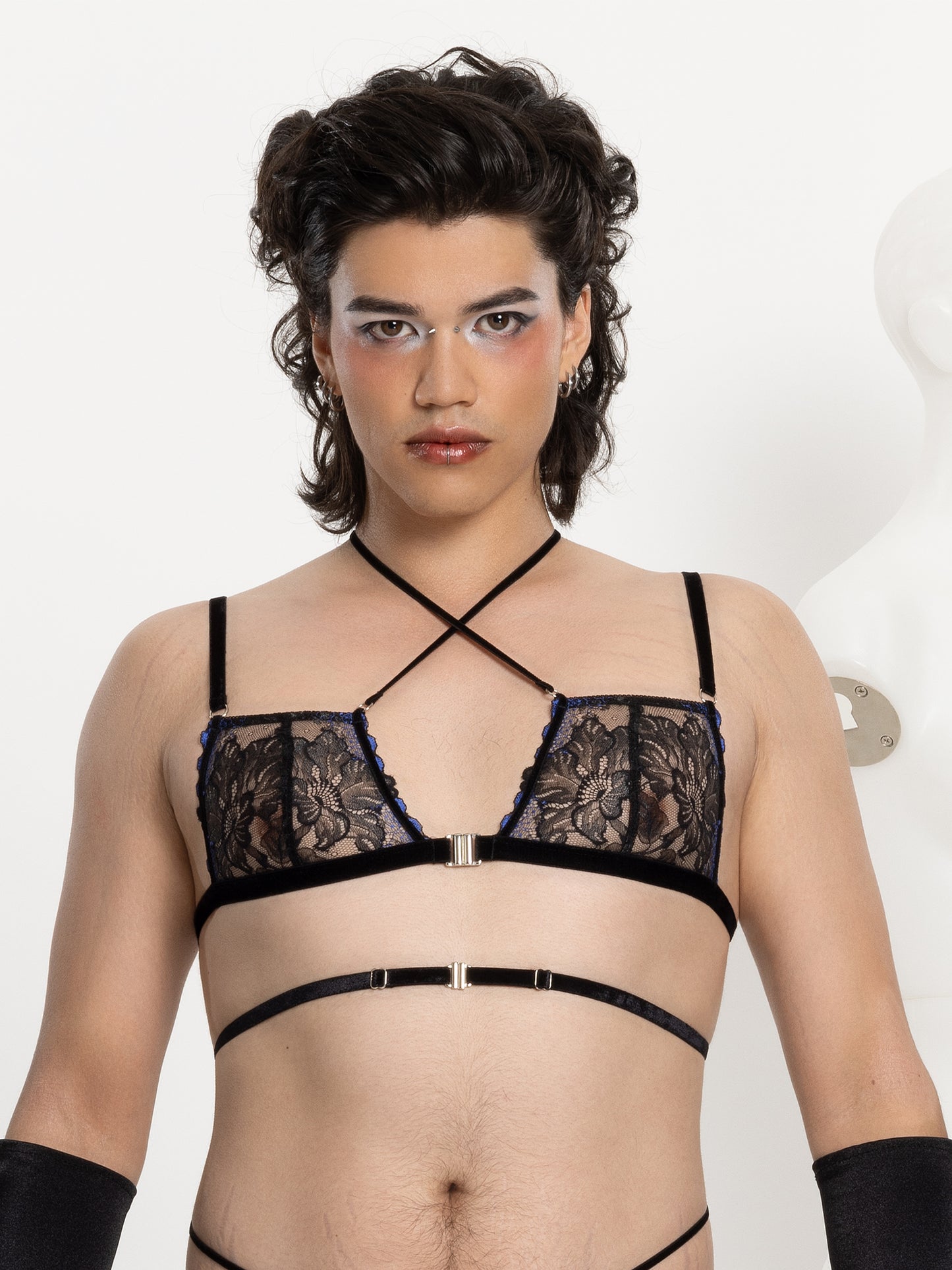 Gender-fluid model wearing a black and blue floral lace bra with velvet straps across the chest and waist and silver front closure.