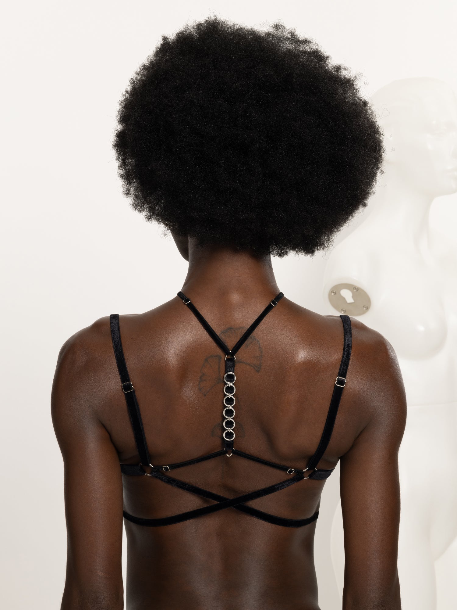 Back view of an adjustable floral lace bra with multiple crossed velvet straps and a silver chain made of 6 o-rings.