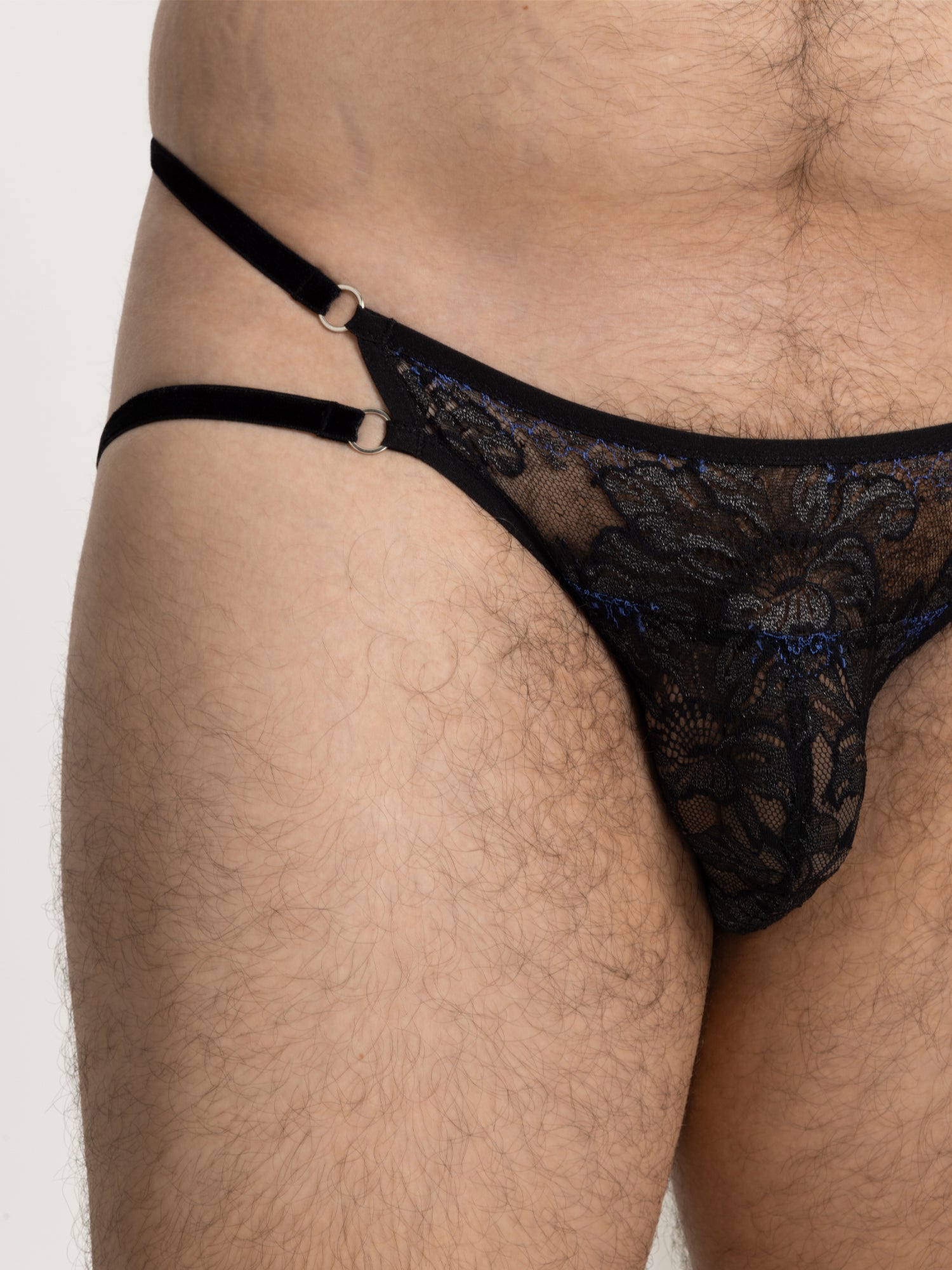 Close up view of black and blue lace pouch fit panties with 2 soft velvet straps on the hip and silver o-ring hardware. 