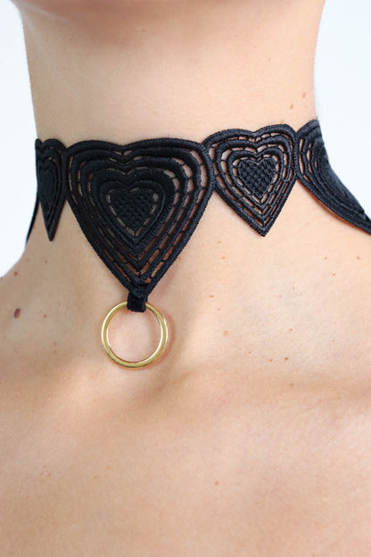 Close up view of a black heart pattern lace choker with a gold o-ring charm.