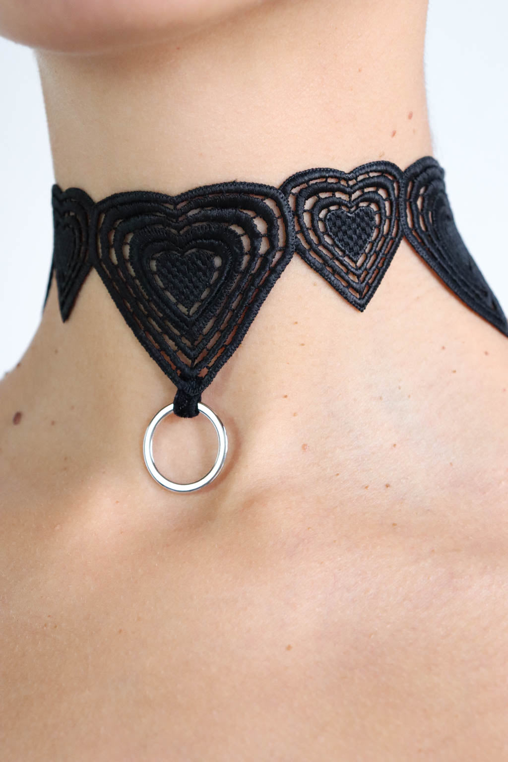 Close up view of a black heart-shaped lace choker with a silver o-ring pendant.