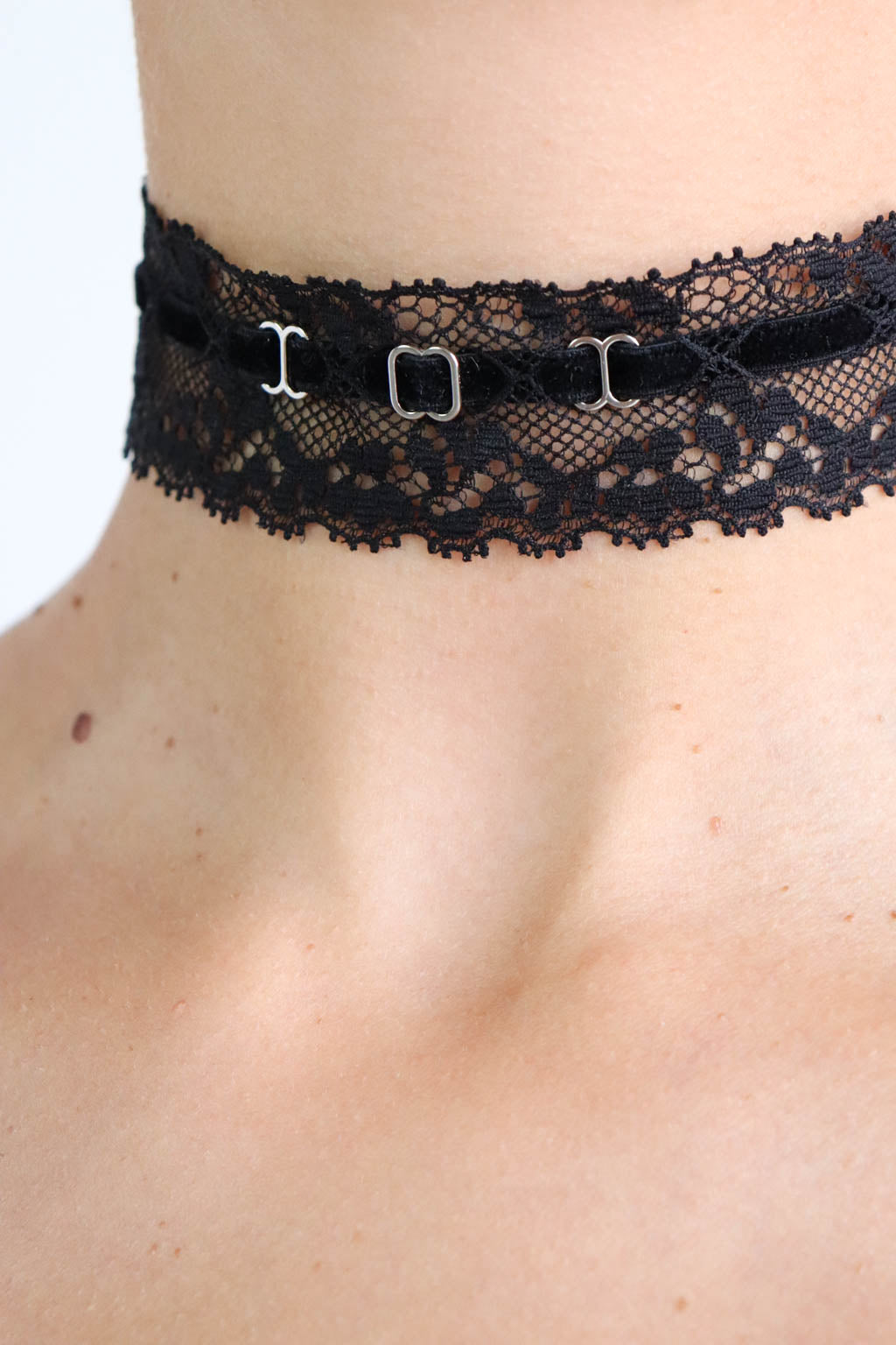 Close up view of a black choker made with lace band, velvet strap and silver hardware. 