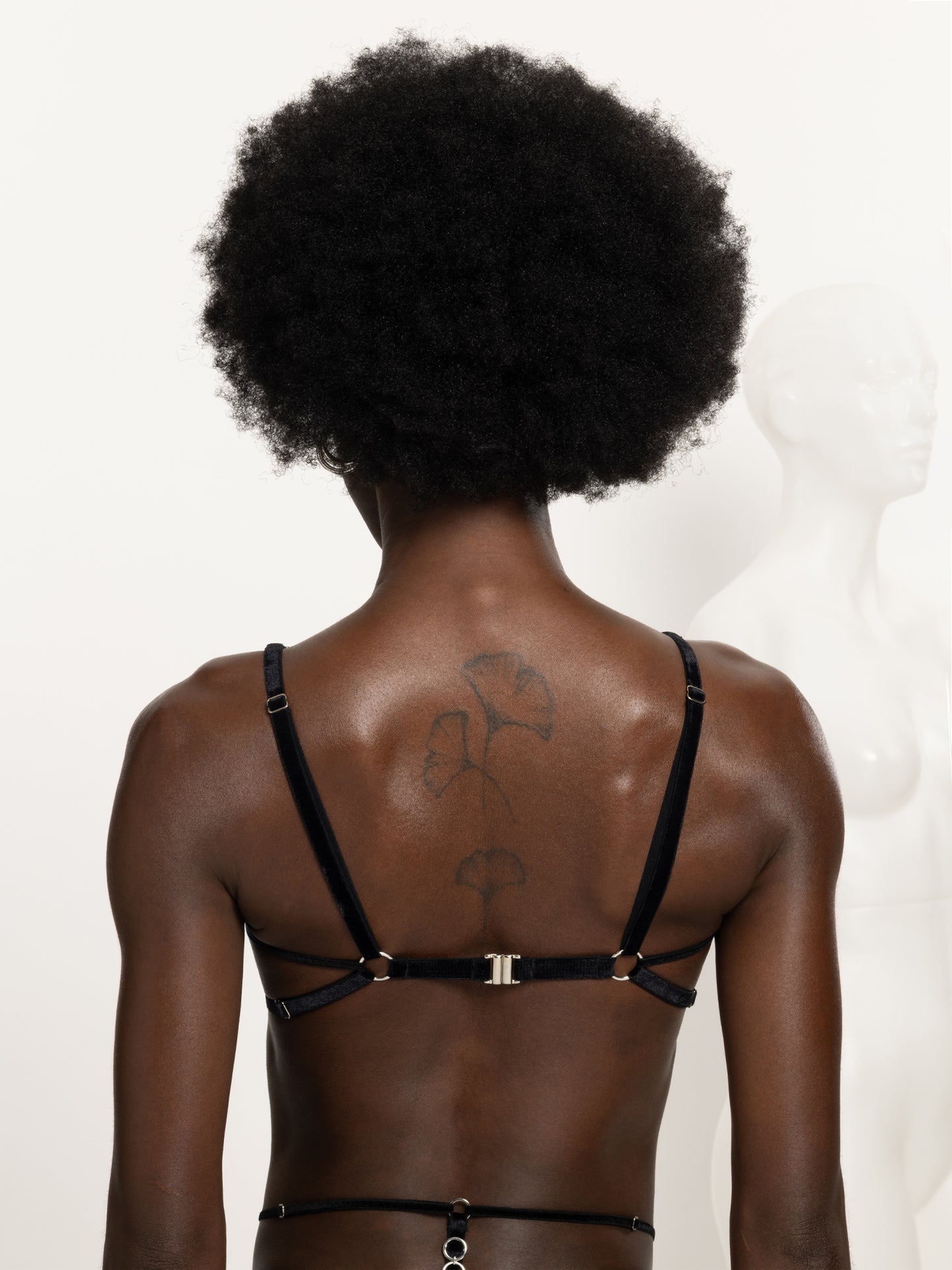 Back view of a model wearing an adjustable black lace and velvet bra harness with silver o-rings details and clasp.