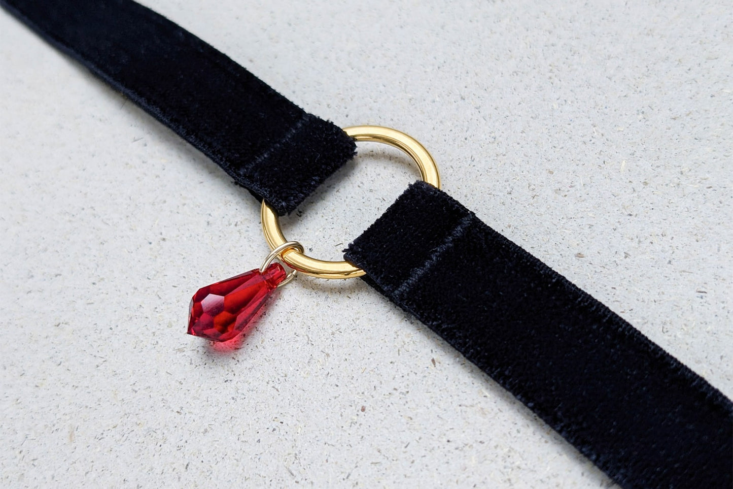 Close up view of a black velvet choker with a gold o-ring jewelry and a red crystal pendant.