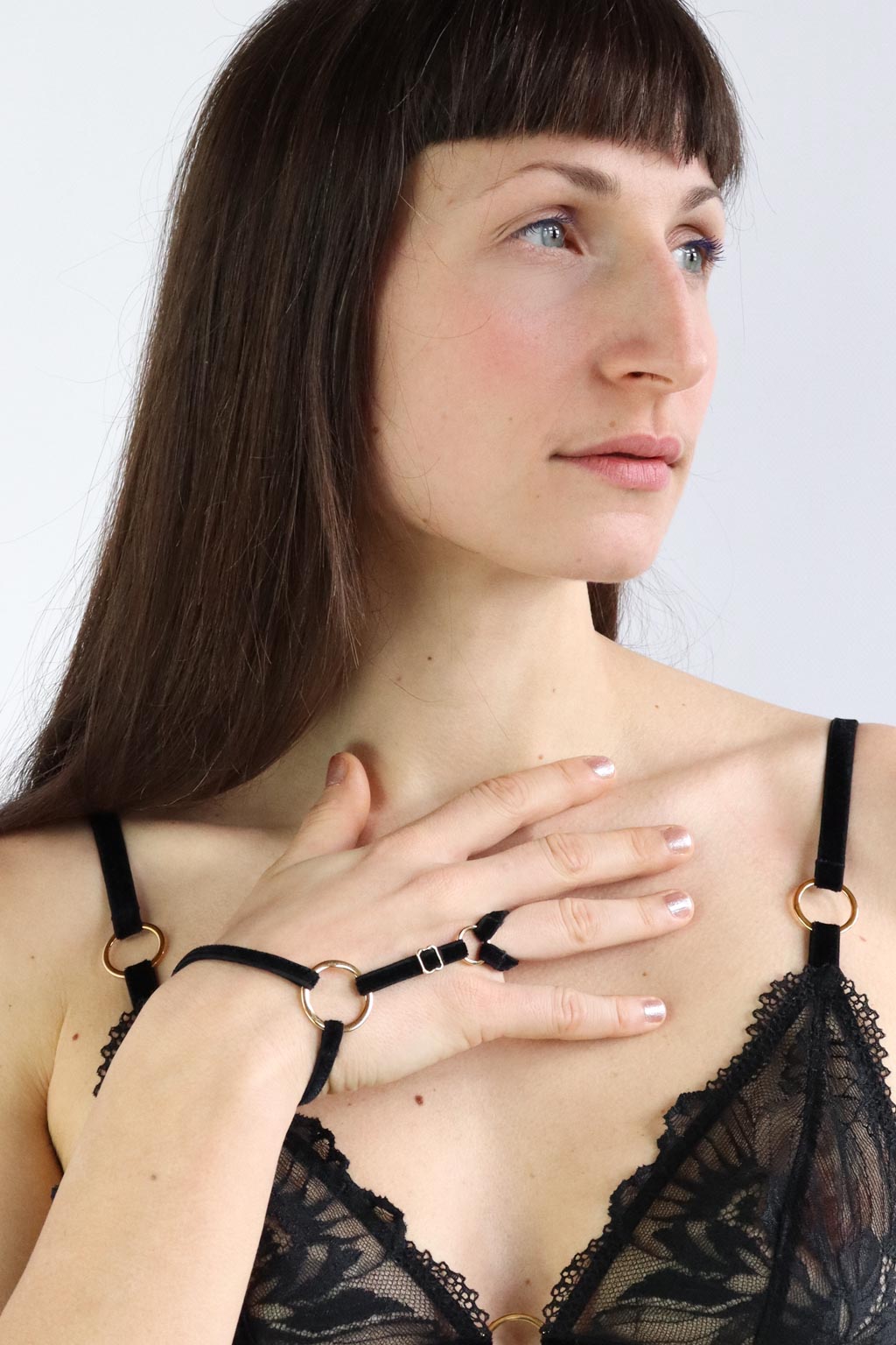 Portrait of a woman wearing a black hand harness with velvet straps around the finger and wrists and gold details.