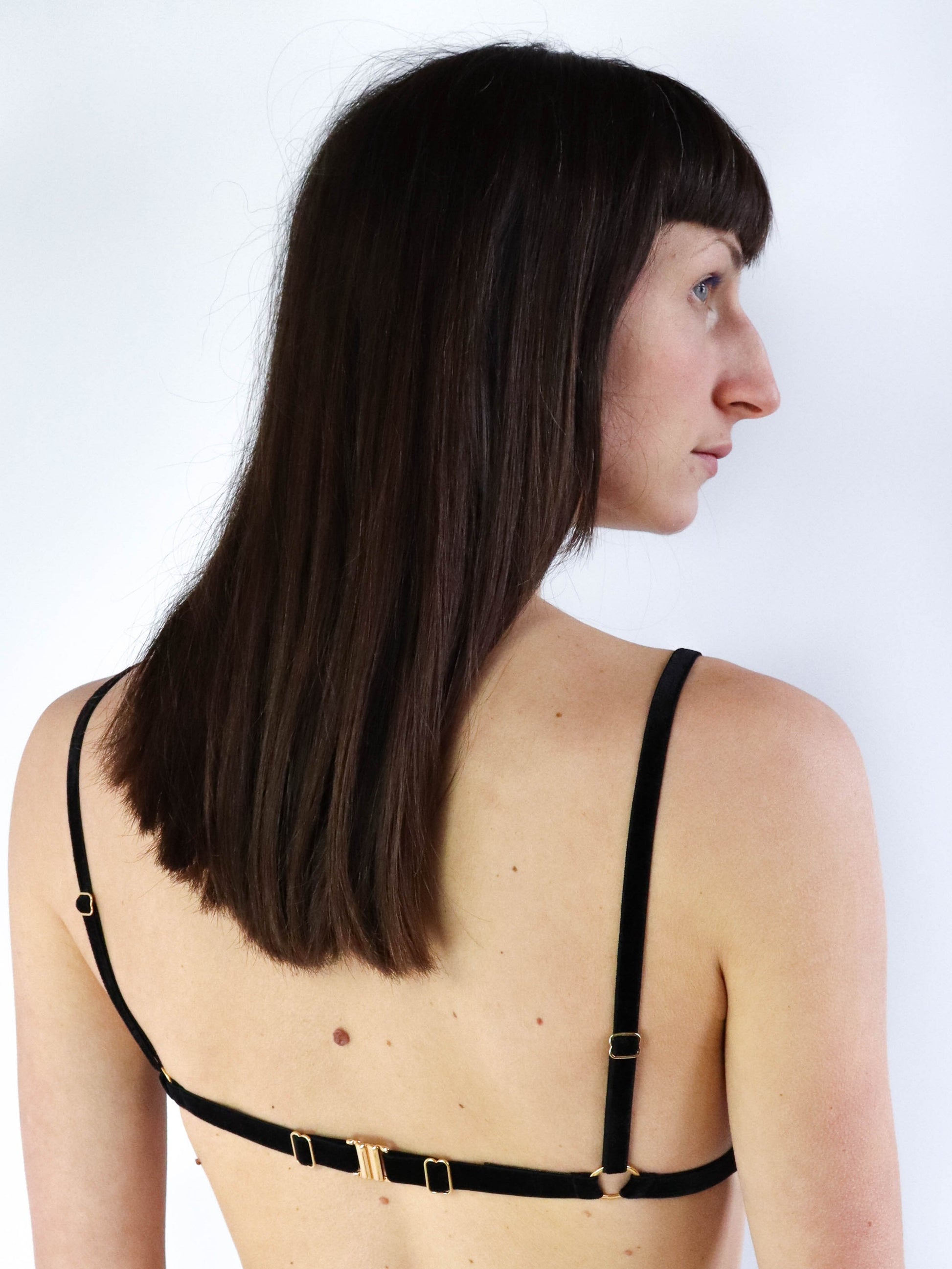 Back view of a model wearing an adjustable black velvet open cup bra with gold clasp.