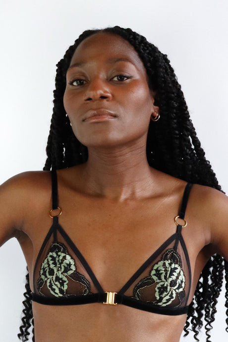 Woman wearing a front closure triangle bra with green and black floral lace, transparent tulle and gold hardware.