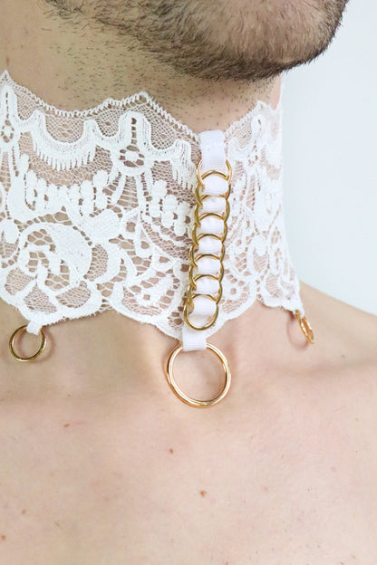 Close up view of unisex collar made of fine white patterned lace and gold o-rings attached.