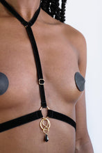 Load image into Gallery viewer, Close-up of a woman wearing a chest harness with black velvet straps, gold hardware and a black crystal pendant.
