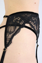 Load image into Gallery viewer, Close-up of the side view of a woman wearing a black floral lace garter belt, with gold hardware.
