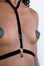 Load image into Gallery viewer, Close-up of a woman wearing a chest harness with black velvet straps, gold hardware and a red crystal pendant.
