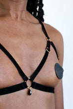 Load image into Gallery viewer, Close-up of a woman wearing an open cup bra harness with black velvet straps, gold hardware and a black crystal pendant.
