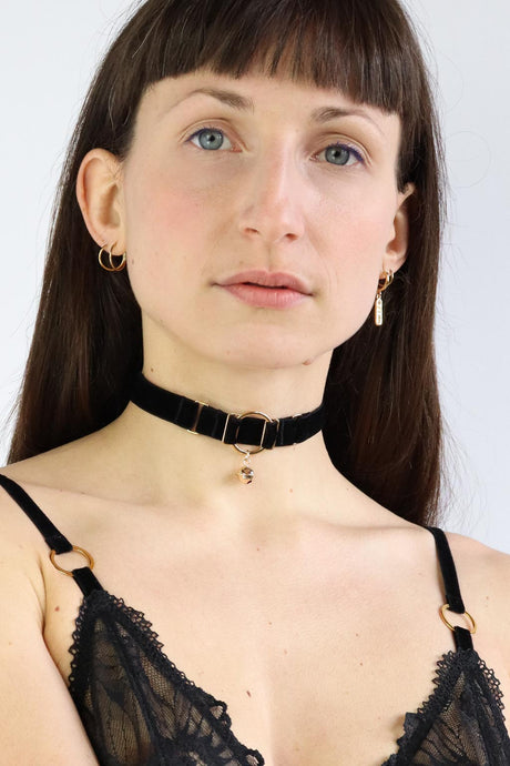 Woman wearing an O-ring black velvet choker with a gold bell charm.