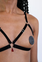 Load image into Gallery viewer, Close-up of a woman wearing an open cup bra harness with black velvet straps, silver hardware and a red crystal pendant.
