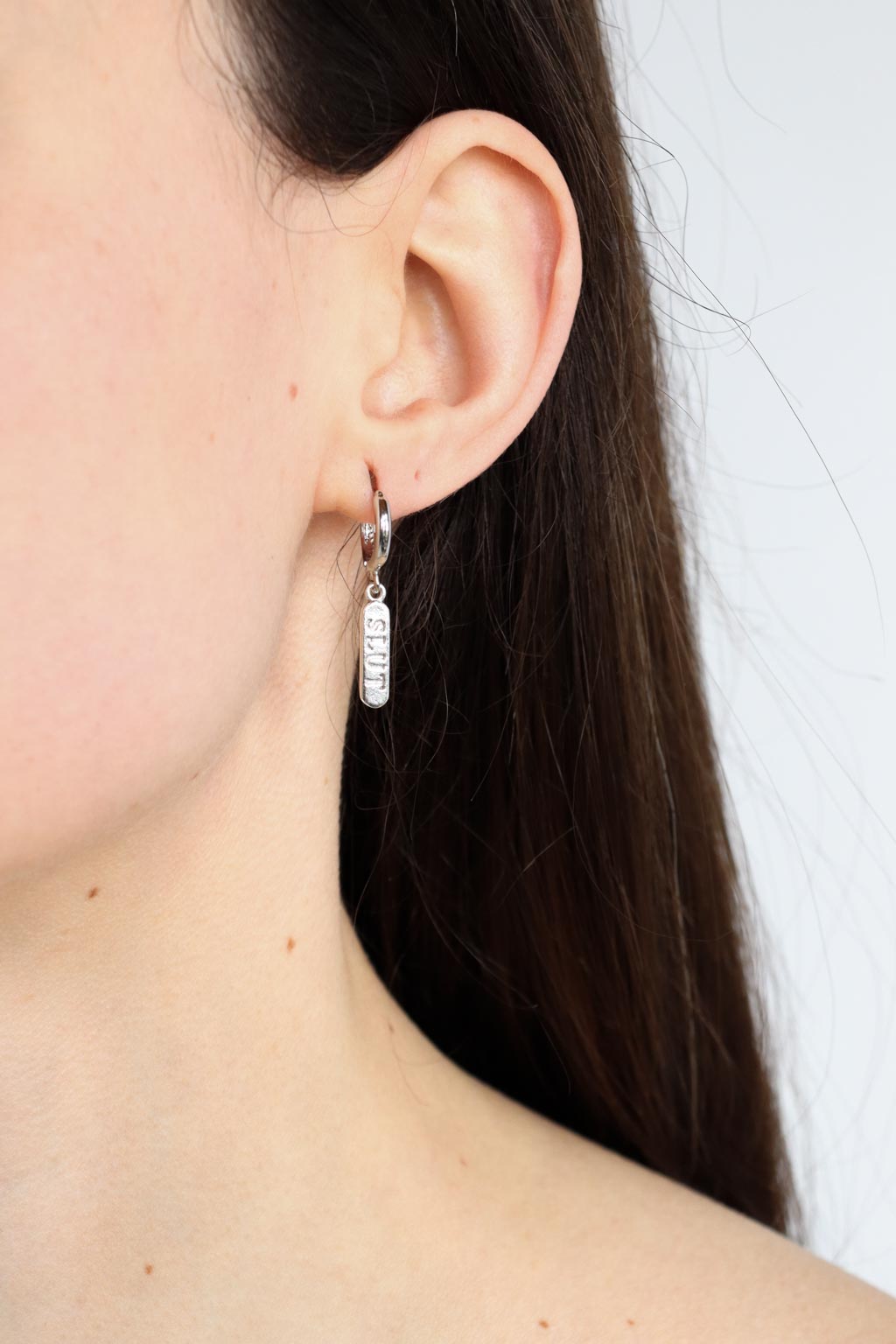 Woman wearing a silver plated huggie earring with a 