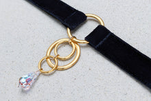 Load image into Gallery viewer, Close-up of an O-ring choker with black velvet straps, gold hardware and a transparent crystal pendant.
