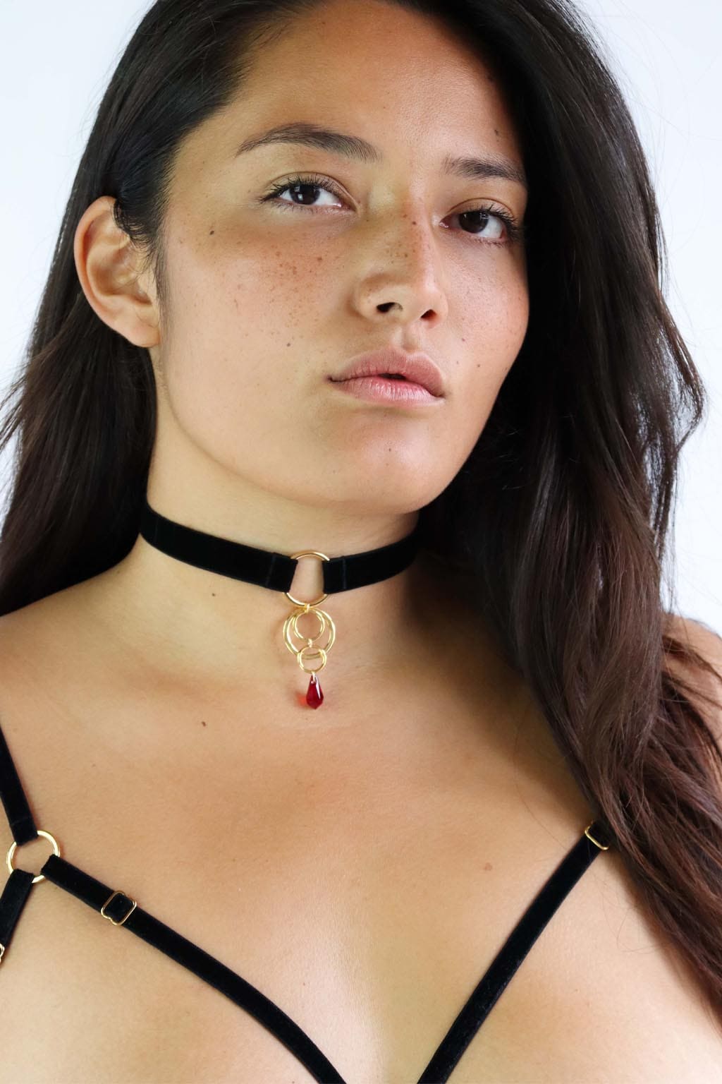 Woman wearing a black velvet choker with a gold 4 O-rings pendant and red crystal.