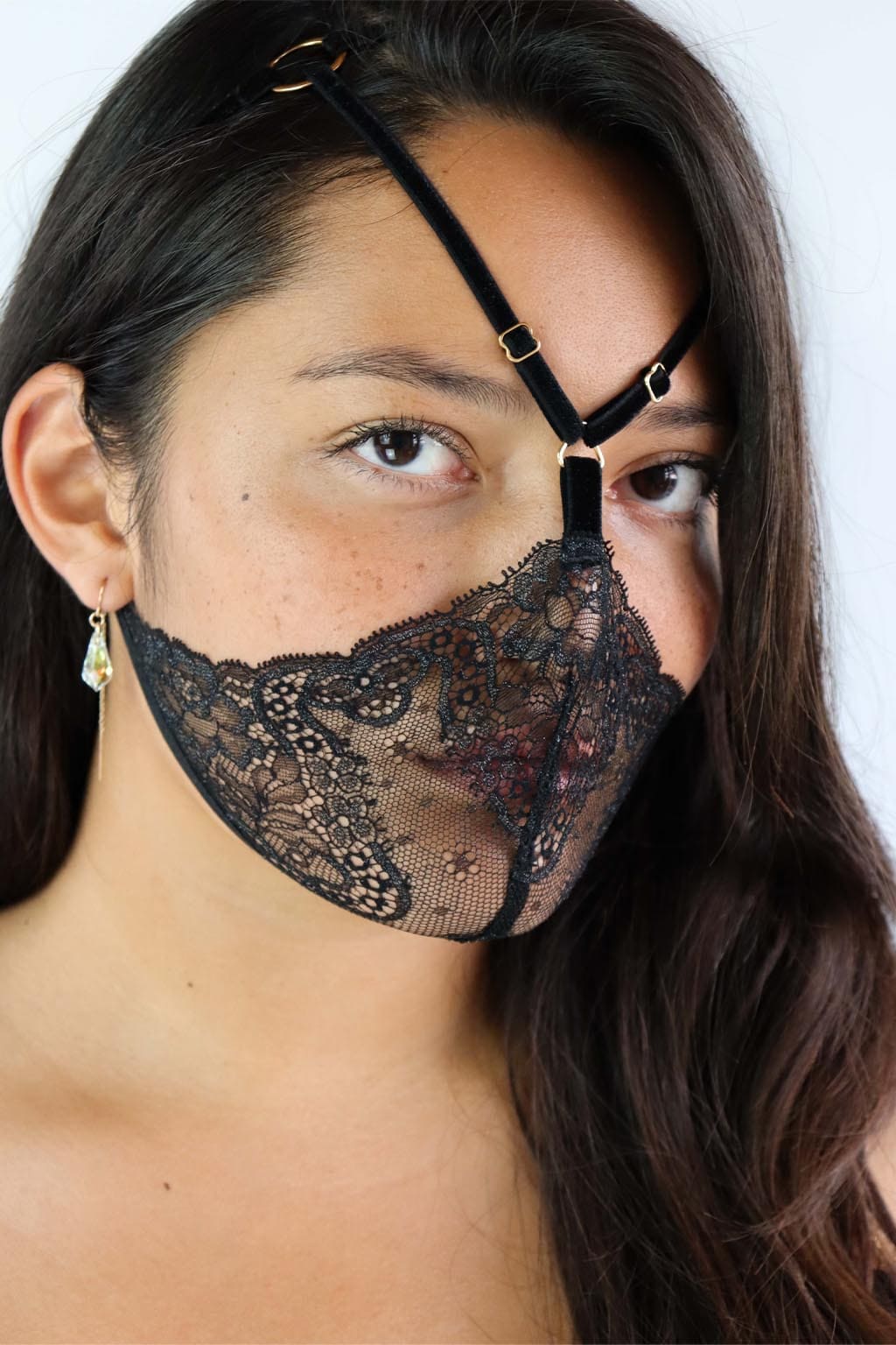 Model wearing a strappy lace face harness, with black lace with silver accents and gold hardware.